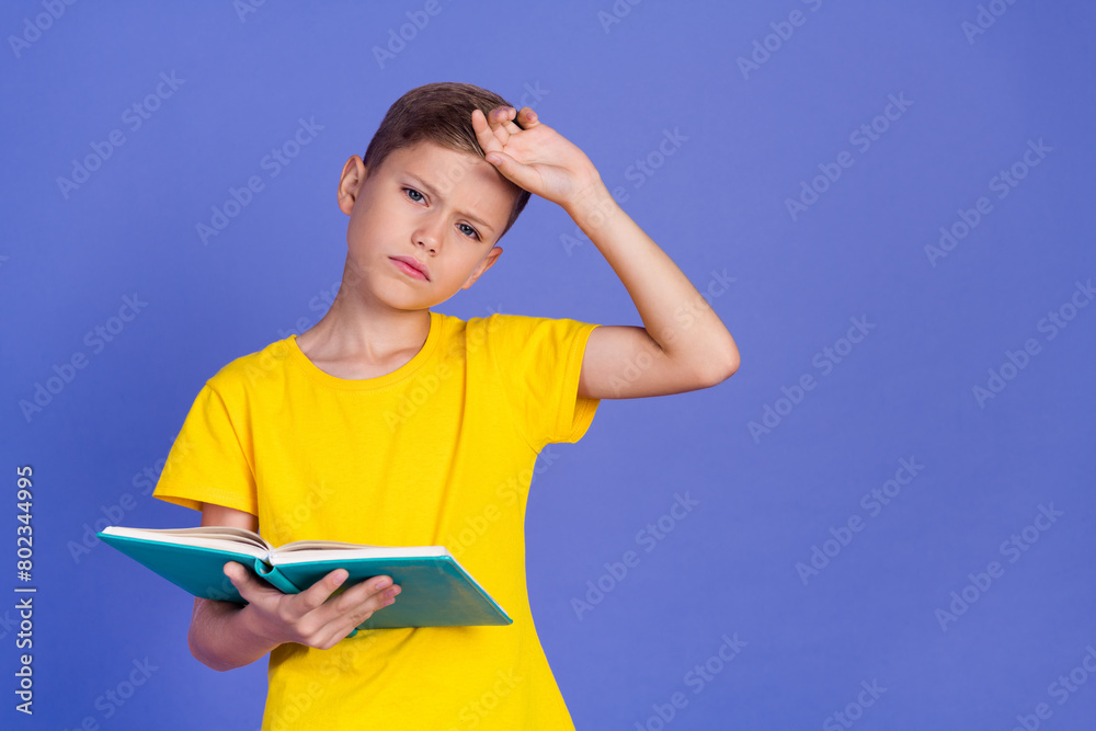 Photo of tired exhausted, clever boy wear stylish yellow clothes hold book touch forehead empty space isolated on purple color background