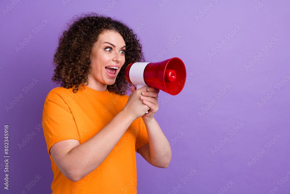 Photo of adorable impressed woman wear orange t-shirt screaming bullhorn empty space isolated purple color background Photo of adorable impressed woman wear orange t-shirt screaming bullhorn empty space isolated purple color background