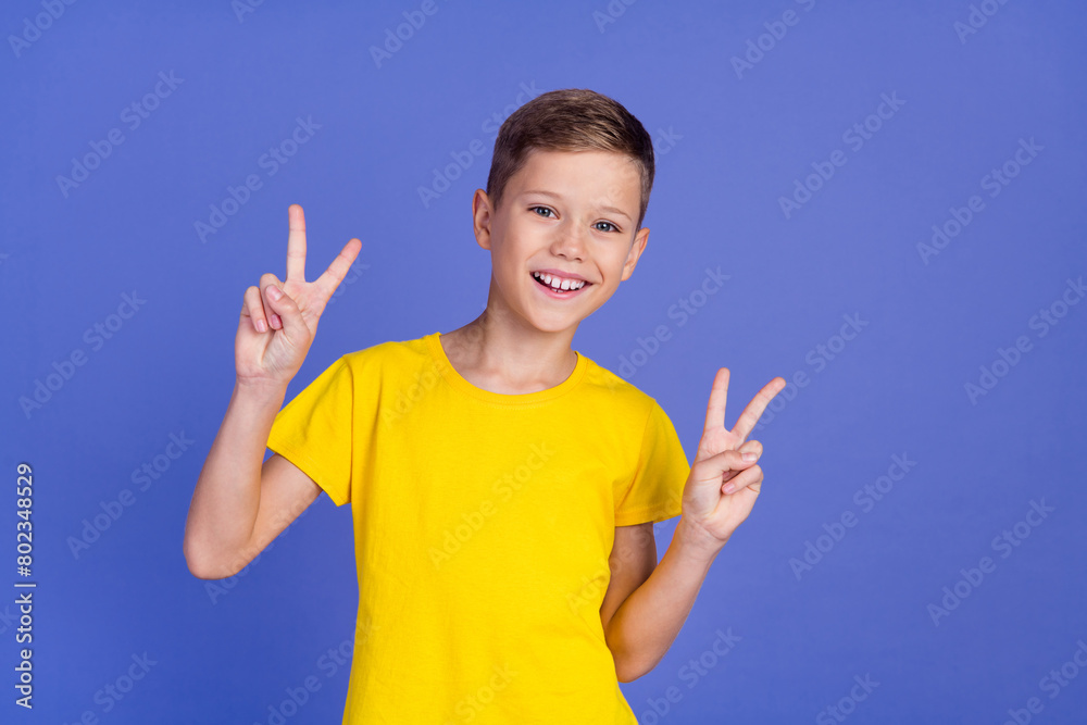 Photo of cheerful glad nice boy wear stylish yellow clothes showing v-sign symbol isolated on purple color background Photo of cheerful glad nice boy wear stylish yellow clothes showing v-sign symbol isolated on purple color background