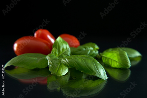 Fresh basil with small tomatoes on black background