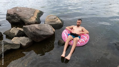 A young man in shorts works on a laptop while swimming in an inflatable ring on the river. Remote work. Freelance.