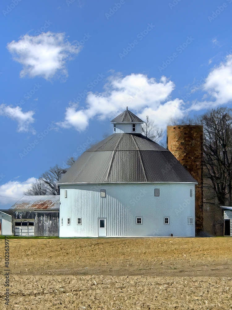 A white round barn on farmland with blue sky and fluffy clouds