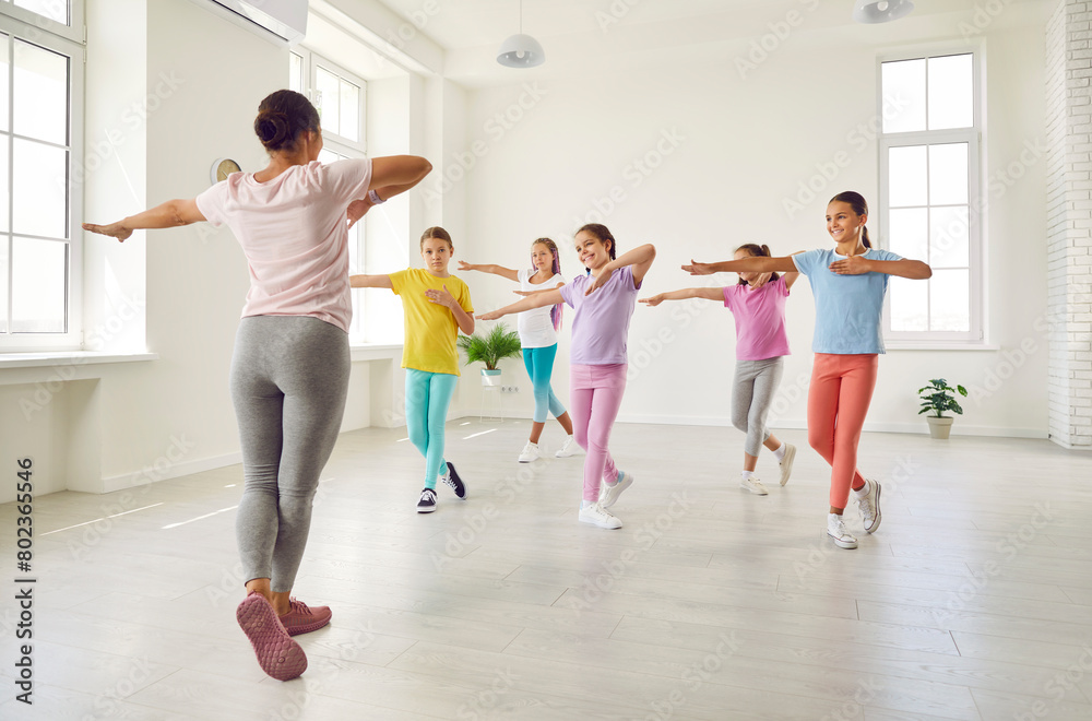 Smiling girls training modern dance moves together in studio with female choreographer. Group of kids doing dance workout in choreography class. Children sport and active lifestyle concept.