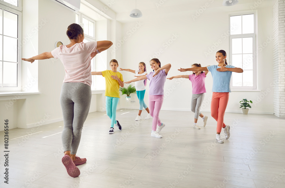 Smiling girls training modern dance moves together in studio with female choreographer. Group of kids doing dance workout in choreography class. Children sport and active lifestyle concept. Smiling girls training modern dance moves together in studio with female choreographer. Group of kids doing dance workout in choreography class. Children sport and active lifestyle concept.
