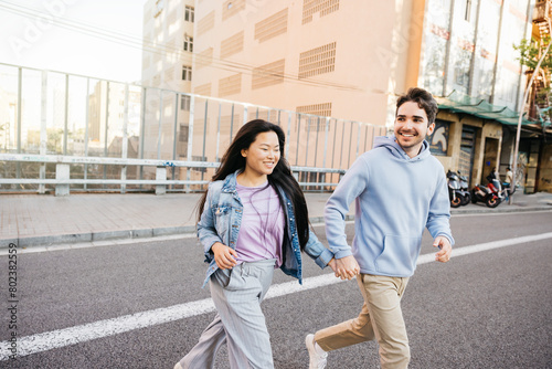 Interracial couple smiling and crossing the road holding hands. Young man and woman running on city street. photo