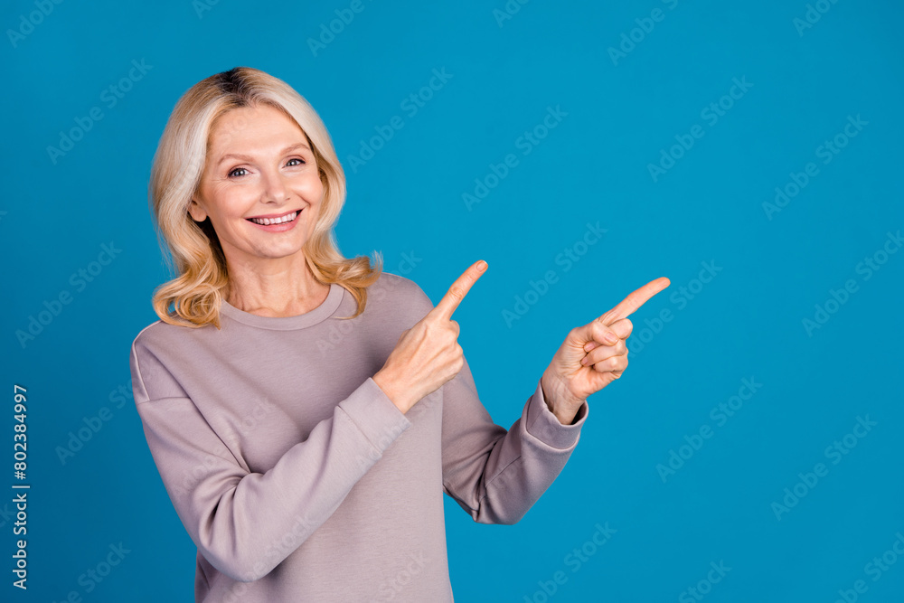 Photo portrait of lovely senior lady point empty space dressed stylish gray garment isolated on blue color background Photo portrait of lovely senior lady point empty space dressed stylish gray garment isolated on blue color background
