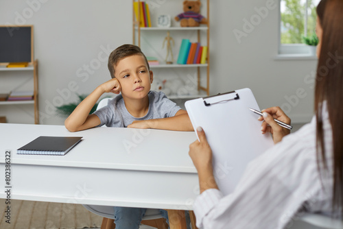 School counselor, psychologist or teacher having conversation with little child boy, holding clipboard, asking questions of personality development test and taking notes. Psychology, education concept photo
