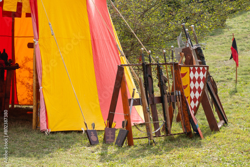 Medieval weapons next to a red yellow tent in a military camp