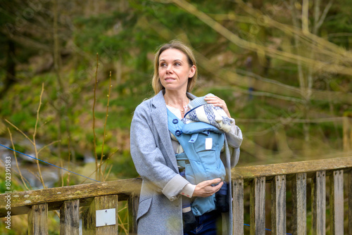 Portrait of a happy woman looking to side while holding and carrying it in a baby carrier standing on a bridge