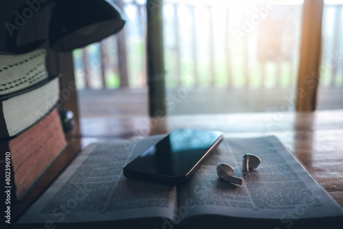 Bible and a smartphone with earphones on wooden table, Christian online technology concept, online live church for sunday service. holy bible book and online study.