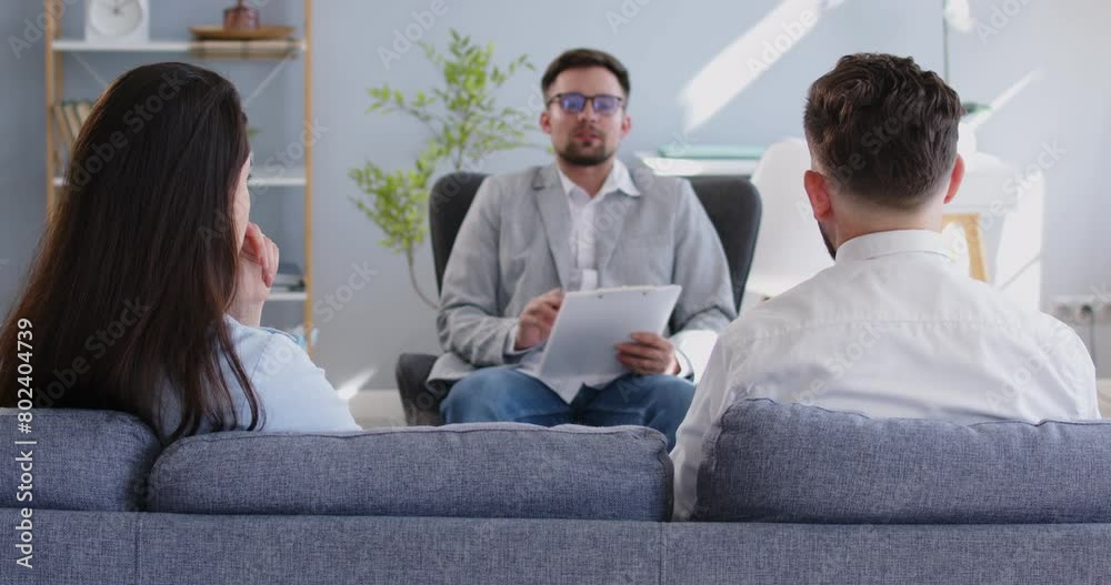 Serious family couple is engaged in communication during a therapy session with a psychologist. The session aims to provide support and consulting for the couple, addressing their serious problems.