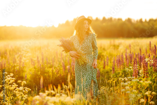 Beautiful woman holding bouquet of lavender flowers walking in summer meadow. Fashion  beauty  nature concept. Collection of medicinal herbs.