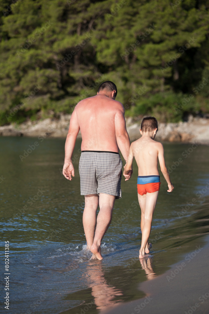 Father and son walking on the beach while holding hands Father and son walking on the beach while holding hands