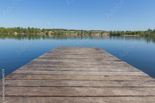 A dock on the lake on the sunny day with nice clean reflection of the forrest behind