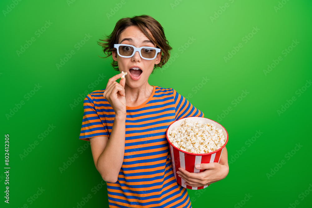 Photo portrait of lovely young lady hold popcorn bucket eating snack dressed stylish striped garment isolated on green color background