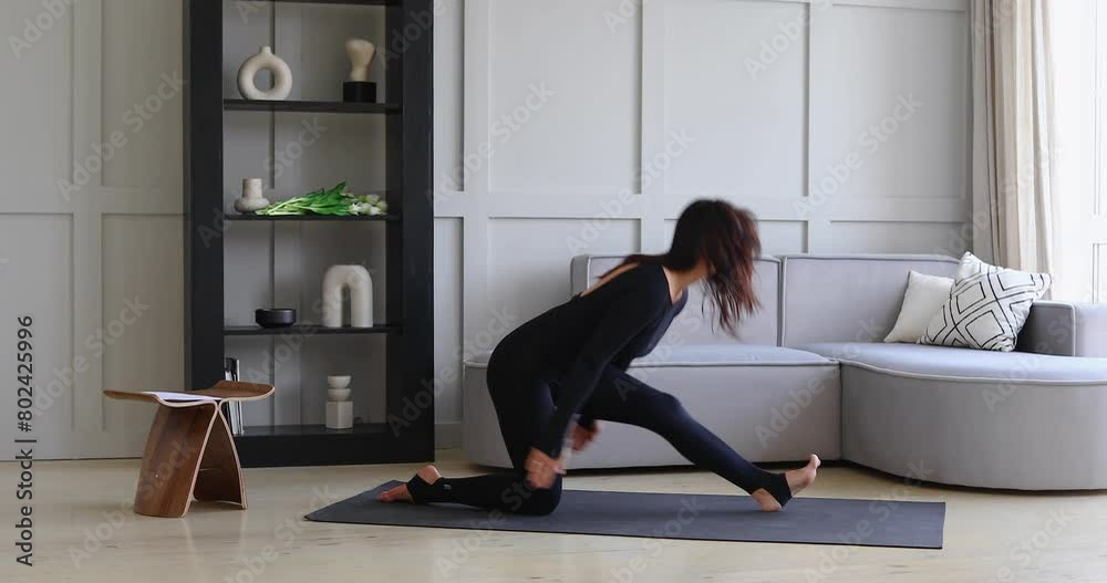 Yoga woman performs dynamic transitions from longitudinal lunge Anjaneyasana to Ardha Hanumanasana, Half Pose of the Monkey King Hanuman, training in black sportswear on a mat in the room