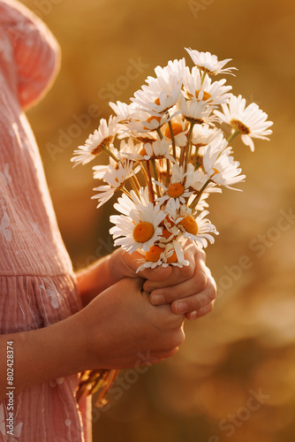 A young girl is holding a bouquet of white flowers. The flowers are arranged in a way that they are all facing the same direction, giving the impression of a unified and harmonious display