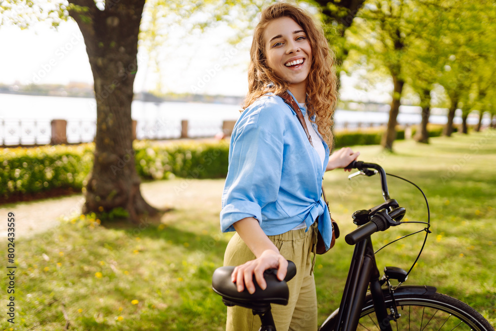Young smiling woman riding bicycle bike on sidewalk in city spring park outdoors. Active urban healthy lifestyle concept. Young smiling woman riding bicycle bike on sidewalk in city spring park outdoors. Active urban healthy lifestyle concept.