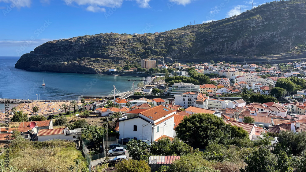 A scenic view of Machico, a coastal town on Madeira Island, with charming houses, lush hills, and the blue waters of the Atlantic Ocean. A scenic view of Machico, a coastal town on Madeira Island, with charming houses, lush hills, and the blue waters of the Atlantic Ocean.