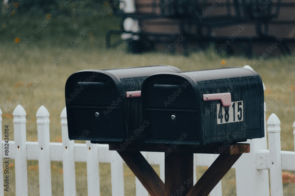 Close-up of mailboxes on a post in front of a white fence Close-up of mailboxes on a post in front of a white fence