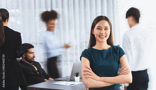 Young Asian businesswoman portrait poses confidently with diverse coworkers in busy meeting room in motion blurred background. Multicultural team works together for business success. Concord