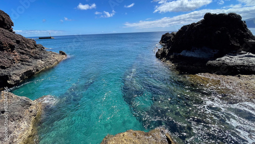 Crystal-clear turquoise waters flow between rocky formations on a sunny day along the coast of Madeira Island