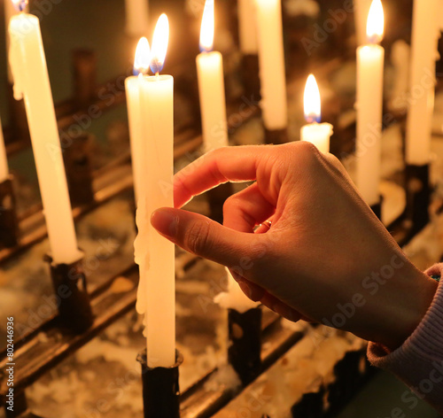 hand lighting a votive candle in the holy place during the religious celebration of the faithful photo