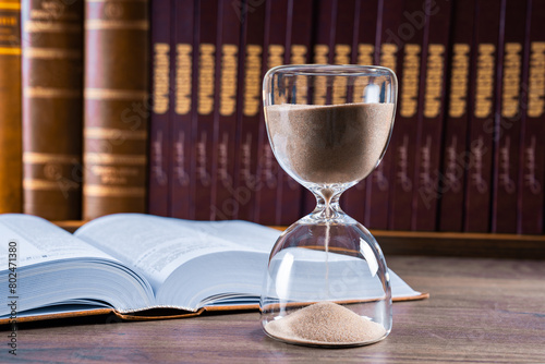 Hourglass and opened book on library table