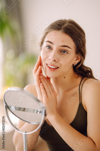 Beautiful woman looking in the mirror, touching her face with her hand, examines acne, pigmentation. Medicine and cosmetology.