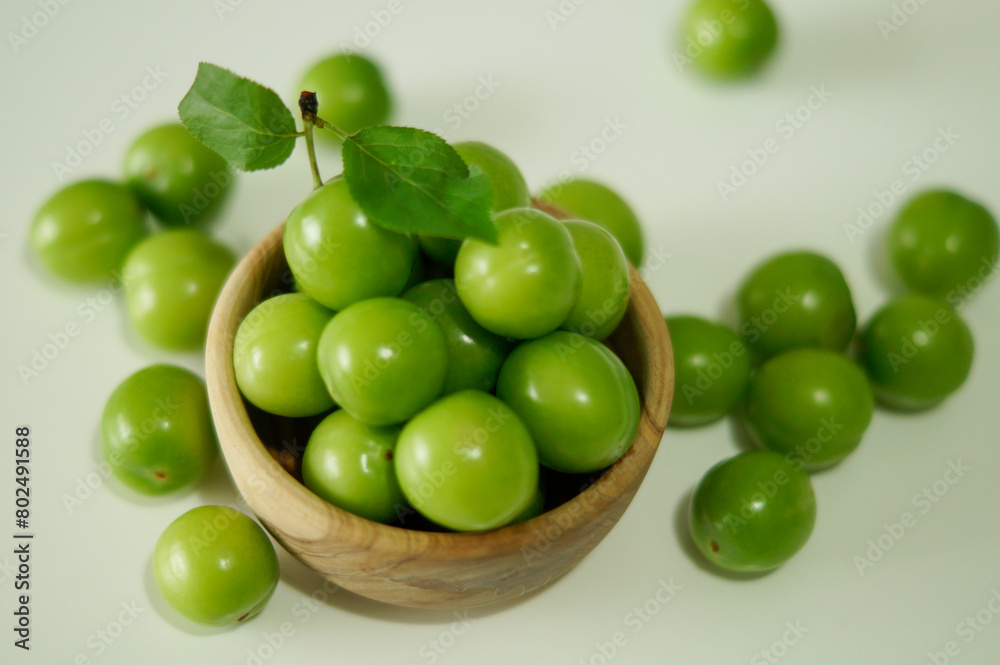 Green plums. A bowl of fresh unripe plums on a white background. Fresh raw green plum in wooden bowl. Top view. Green plums. A bowl of fresh unripe plums on a white background. Fresh raw green plum in wooden bowl. Top view.