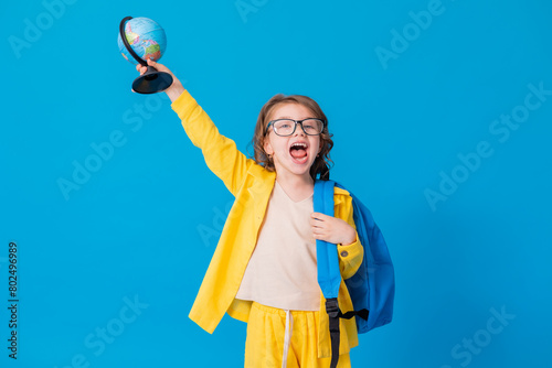 schoolgirl girl in a yellow suit on a blue background with eyeglasses and a globe in her hands