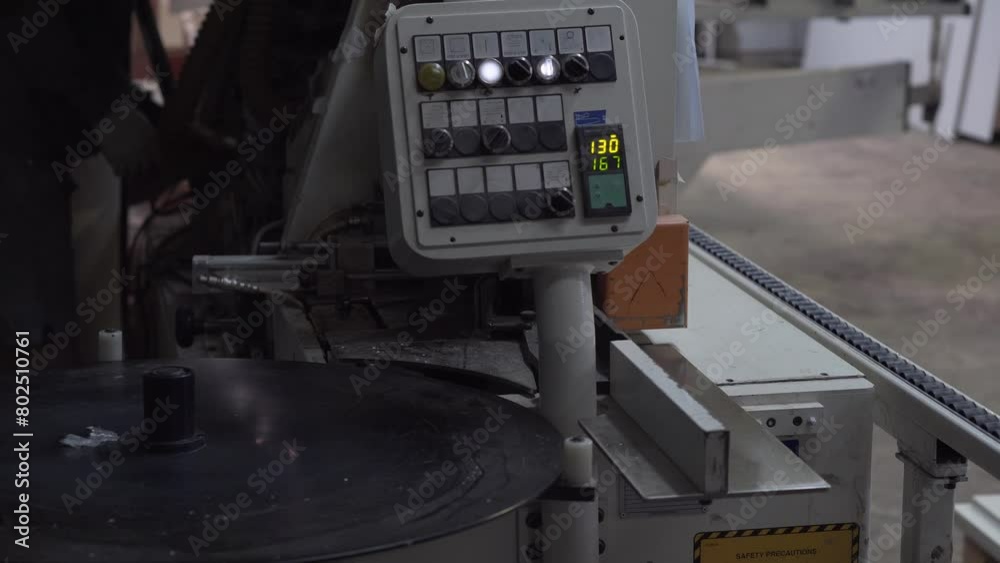 Automatic edge bander on furniture production. Worker adjusts the woodworking machine in the background. Automatic edge bander on furniture production. Worker adjusts the woodworking machine in the background.