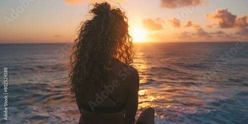 Captivating curly-haired woman enjoys vibrant sunset at sea, evoking peaceful vacation vibes, golden and blue hues dominate, one person. Copy space. © BrightWhite