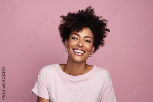 A woman with curly hair is smiling and wearing a pink shirt