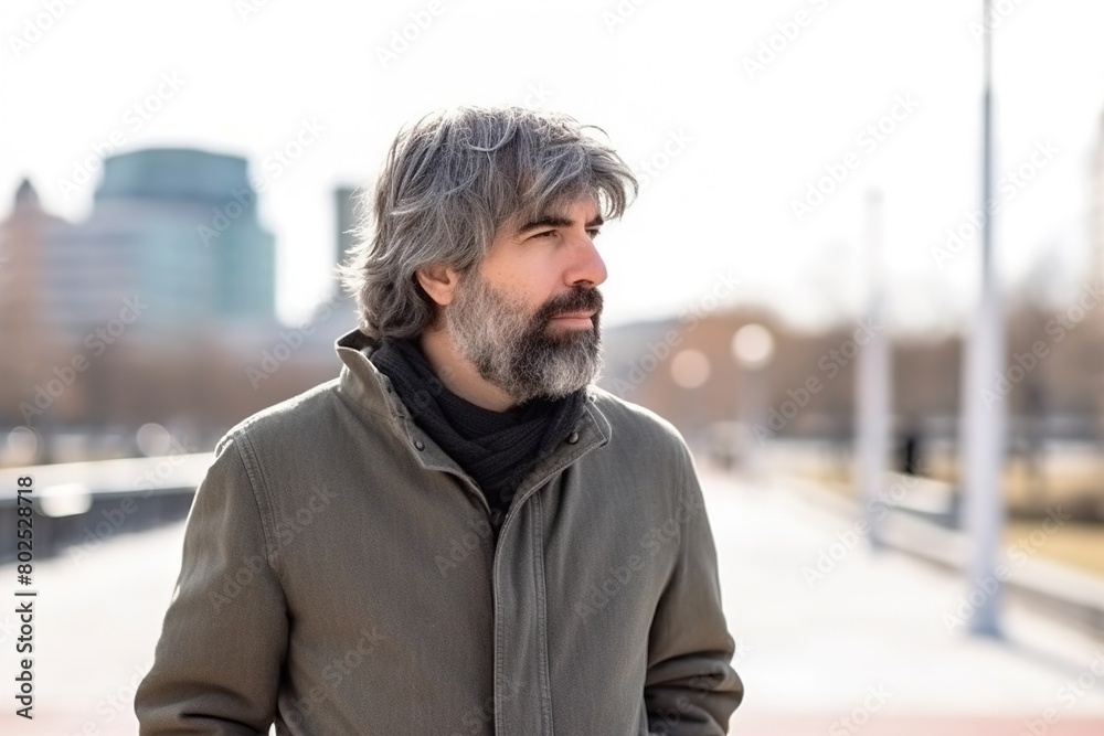 A man with a beard and gray hair is standing on a sidewalk A man with a beard and gray hair is standing on a sidewalk