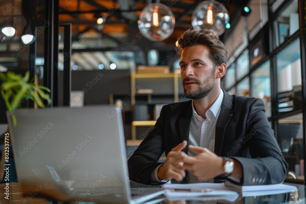 A professional man in a suit focuses intently on his laptop in a modern cafe setting A professional man in a suit focuses intently on his laptop in a modern cafe setting