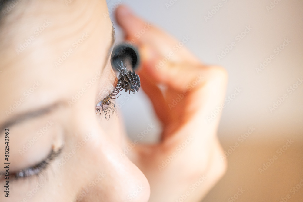 Obraz premium Detail of a young teenager in profile applying mascara to her eyes. The light is warm and soft.