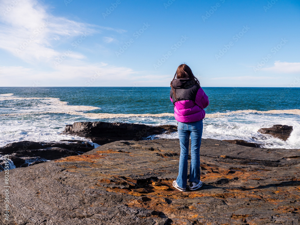 Teenager girl enjoy stunning nature of Kilkee coast and cliff, county Clare, Ireland. Rough coastline and blue cloudy sky. Travel and tourism. Irish landscape scene. Warm day.