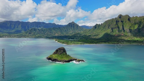 Breathtaking drone shot captures a Chinese hat rock in the midst of blue ocean waters, framed by dramatic green mountain ranges on a sunny day. Hawaii islands, Oahu, Honolulu, USA.  photo