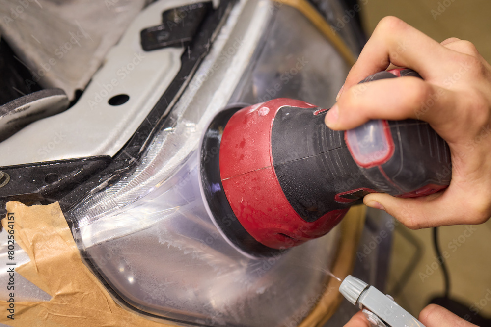 Person using a machine to polish automotive lighting on a car headlight Person using a machine to polish automotive lighting on a car headlight