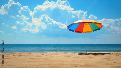 A vibrant beach umbrella provides shade on the sandy shore overlooking the sparkling ocean  with people enjoying the coastal natural landscape under a clear sky AIG50