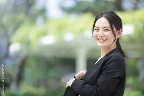 屋外でスーツを着た若い女性　営業や外回り、新卒などのイメージ　カメラ目線　左にコピースペースあり