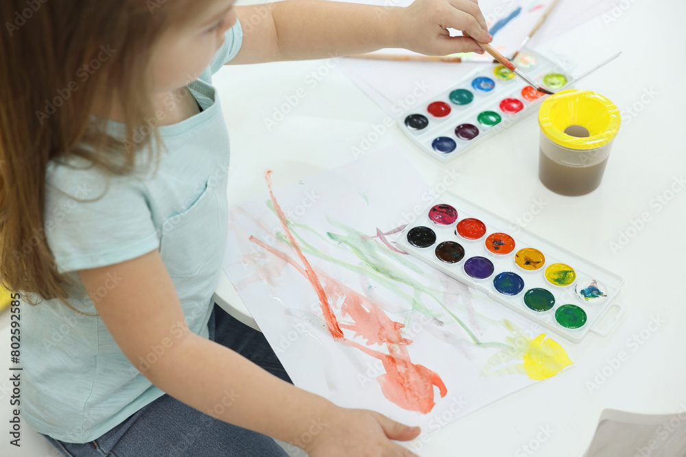 Little girl painting with brush and watercolor at white table, closeup Little girl painting with brush and watercolor at white table, closeup