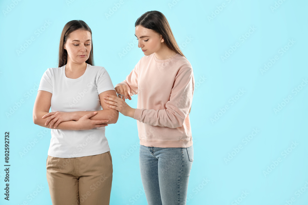 Woman giving insulin injection to her diabetic friend on light blue background Woman giving insulin injection to her diabetic friend on light blue background
