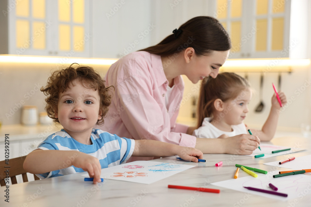 Mother and her little children drawing with colorful markers at table in kitchen Mother and her little children drawing with colorful markers at table in kitchen