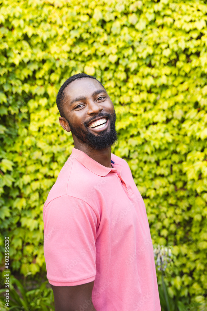 African American man standing outdoors, smiling in front of green plants African American man standing outdoors, smiling in front of green plants