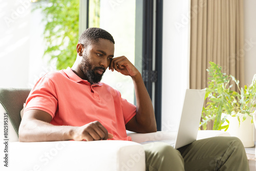 At home, African American man in pink shirt and green pants examining laptop screen photo
