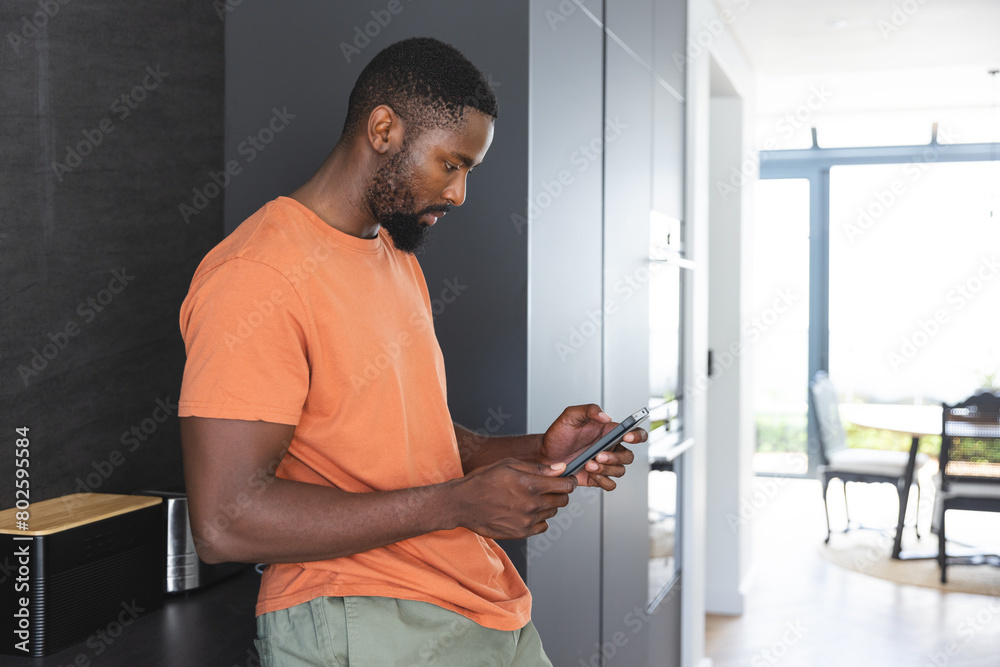 At home, African American male checking smartphone, wearing orange shirt At home, African American male checking smartphone, wearing orange shirt