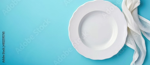 White plate and cloth napkin placed on a blue background. Ideal background for menu and recipe book covers, showcasing a table setting in a flatlay, top-down view.