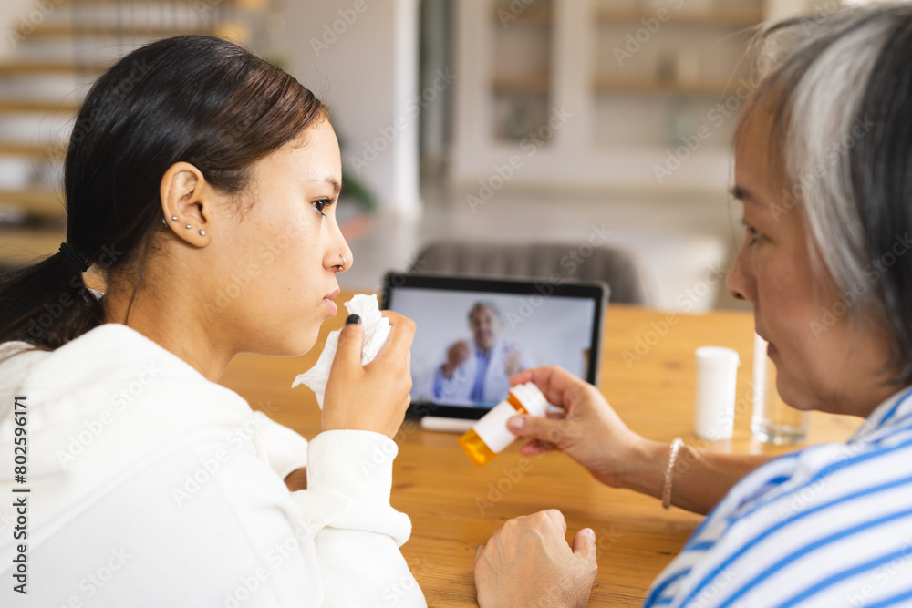 Asian grandmother and biracial granddaughter video calling at home, one blowing nose Asian grandmother and biracial granddaughter video calling at home, one blowing nose